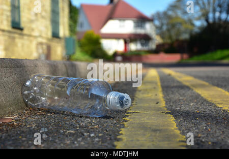 Un scartato la bottiglia di plastica si trova nella gronda a lato di una strada urbana con linee gialle Foto Stock