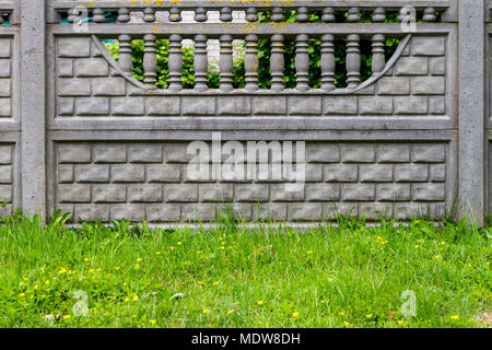 Frammento di recinzione in cemento con motivi decorativi su un prato verde. Architettura di sfondo di dettaglio Foto Stock