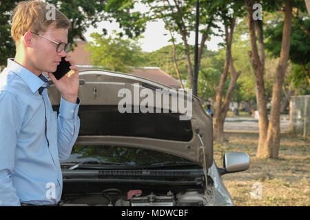Agente maschio utilizzare smart phone per rivendicare assicurazione auto. uomo caucasico che chiamano per richiedere assistenza per auto danneggiato da incidente stradale Foto Stock