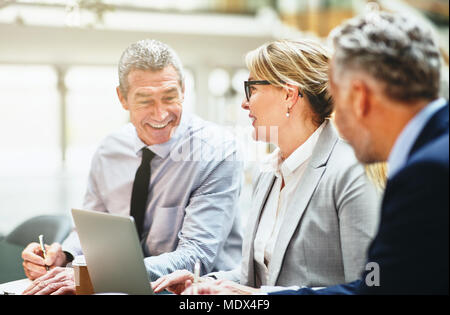 Tre imprenditori matura sorridente e parlare insieme durante una riunione in una tabella in un ufficio moderno Foto Stock
