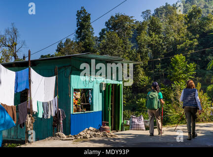 Due donne a camminare su una strada oltre una casa colorata e uno stendibiancheria; West Bengal, India Foto Stock