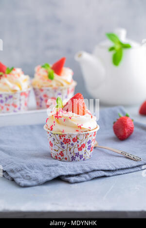 Muffin fatti in casa o i tortini con panna alla vaniglia e fragole fresche su sfondo grigio chiaro, con un copyspace Foto Stock