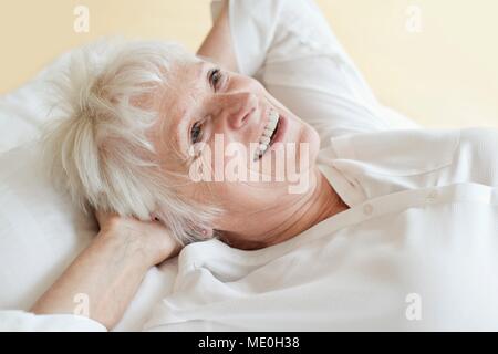 Senior donna sdraiata con le mani dietro la testa. Foto Stock