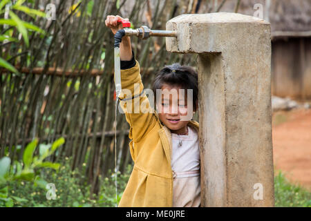 Ragazza Hmong giocando con un rubinetto di acqua in Na Kam Peng, chiamato anche il villaggio di bomba, Xiangkhouang, Laos Foto Stock