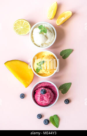 Tre diversi tipi di frutta e bacche di gelati su sfondo rosa, copia dello spazio. Frozen yogurt o un gelato al limone, mango, mirtilli - estate sani Foto Stock