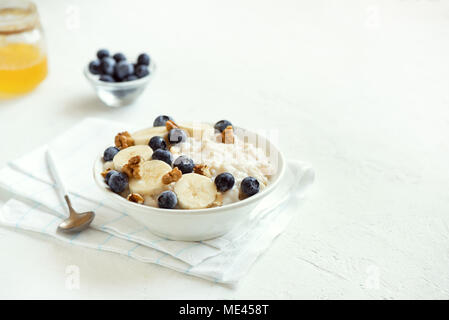 Farina di avena porridge con noci, mirtilli e banana in vaso - sana prima colazione biologica, avena con frutta, miele e noci Foto Stock