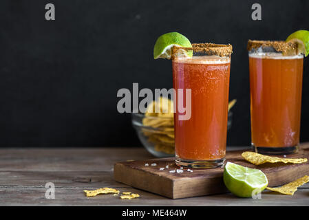 Michelada (messicano sanguinosa birra) con Spisy Rim e il succo di pomodoro è servita con tigli e Nacho Chips. Estate Cocktail alcolici Michelada. Foto Stock