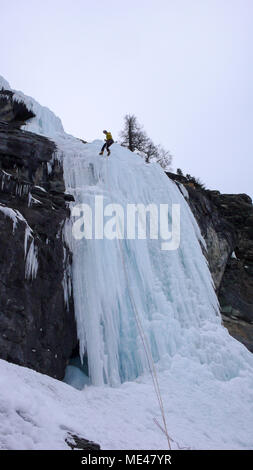 Maschio guida di montagna rappelling off di una ripida cascata ghiacciata in una fredda giornata invernale nelle Alpi Foto Stock