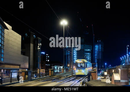 Il tram a Rochdale entrando nel centro della città di Manchester a pernottamento con alti edifici e costruzione di gru in background di notte Foto Stock