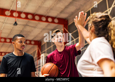 Gruppo di adolescente amici su un campo da basket dando a ogni altro un alto cinque Foto Stock