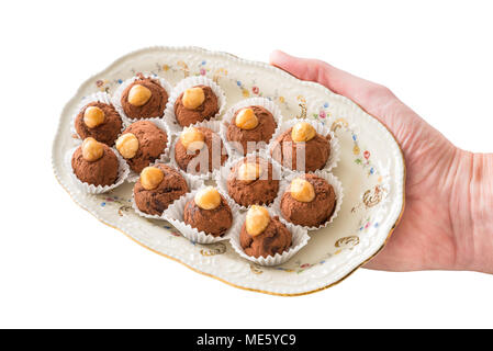 Cioccolato artigianale bomboni con nocciola intera in una piastra ellittica tenuto in mano, su sfondo bianco. Messa a fuoco selettiva Foto Stock