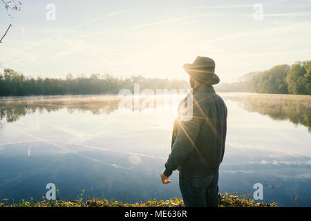 Giovane uomo di contemplare la natura in riva al lago di sunrise, primavera, in Francia, in Europa. Persone Viaggi relax nella natura del concetto. Immagine dai toni Foto Stock