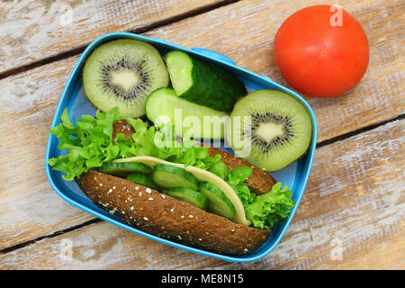 Scuola di sano pranzo scatola contenente formaggio marrone sandwich, bastoncini di cetriolo, pomodoro e kiwi Foto Stock