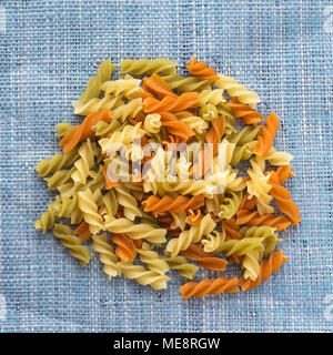 Materie spirale colorata una manciata di maccheroni su un rustico a maglia blu sacco texture. Vista da vicino dall'alto. Foto Stock