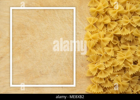 Farfalle maccheroni bella di cui la pasta con la destra, vista laterale su un tavolo di legno al top con un background testurizzato. Vista da vicino dall'alto. Con cornice bianca per il testo. Foto Stock