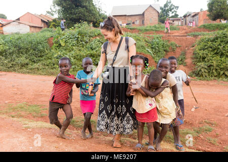 Lugazi, Uganda. 17 maggio 2017. Un bianco-pelato volontario (denominata 'mzungu' o 'muzungu' localmente) tenendo le mani con bambini ugandesi in una zona rurale. Foto Stock