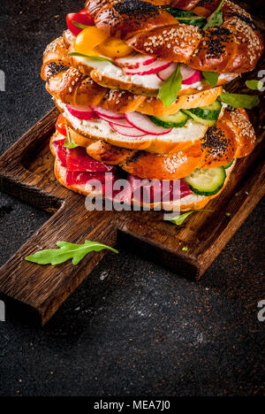 Pila di varie ciambelle fatte in casa panini con sesamo e semi di papavero, crema di formaggio, prosciutto, radicchio, rucola, pomodori ciliegini, cetrioli, del taglio b Foto Stock