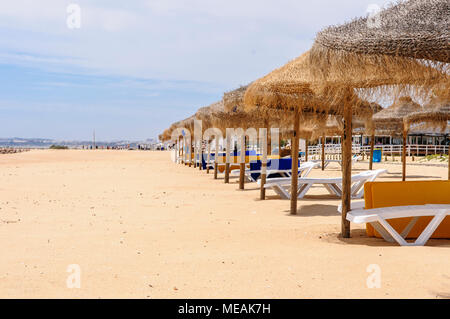 File di paglia di ombrelloni e sedie a sdraio sulla spiaggia di Vilamoura, Algarve, Portogallo. Foto Stock