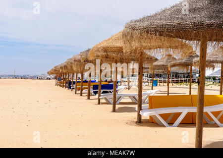 File di paglia di ombrelloni e sedie a sdraio sulla spiaggia di Vilamoura, Algarve, Portogallo. Foto Stock