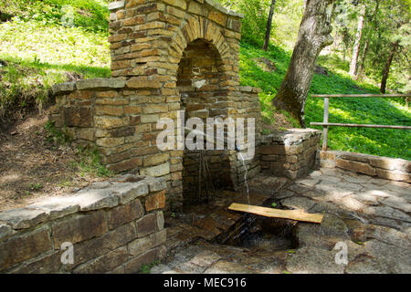 Acqua in un tubo da una molla in una parete di pietra Foto Stock