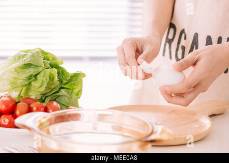 Mani femminili è bombardare le uova di gallina. La donna si prepara la colazione a casa. Bollite le uova di gallina in legno ware al buio su un tavolo. Tonificazione vintage Foto Stock