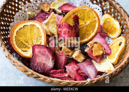 Frutti essiccati misti arancia, fragola, ananas, ciliegia e fette di mela con cannella in polvere nella cesta in legno. Alimenti biologici. Foto Stock