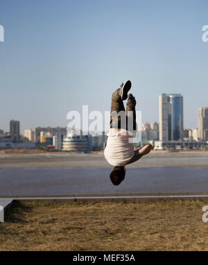 Giovane maschio sportivo acrobatico esegue trucchi capovolto nella parte anteriore della skyline Foto Stock