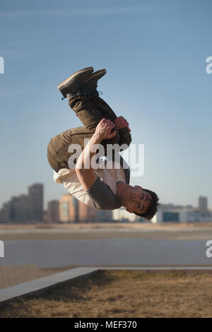 Giovane uomo sportivo parkour esegue trucchi nella parte anteriore della skyline Foto Stock