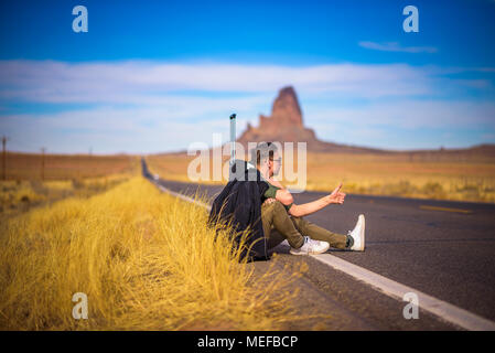 Stanco sollevatore-escursionista con la valigia seduto su una strada Foto Stock