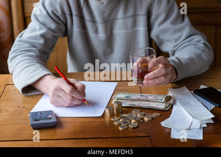 Chiudere l'uomo con la calcolatrice di conteggio, rendendo note a casa, la mano è scrive in un notebook. Monete impilate disposte a deesk. Risparmi il concetto di finanze. Foto Stock