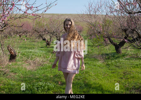 Bionda in abito rosa passeggiate nel giardino con alberi in fiore Foto Stock