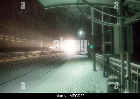 Sera treno arriva alla stazione. Nevicata complica il trasporto di passeggeri, blocchi di neve. Blizzard e derive di neve Foto Stock