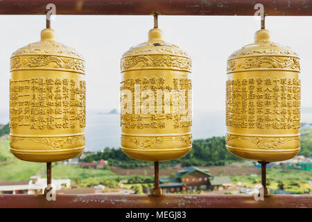 Tre golden ruote della preghiera al tempio Sanbanggulsa con vista sulla costa, Sanbang-ro, Jeju Island, Corea del Sud Foto Stock