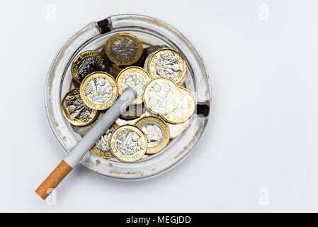 Sigarette e British Pound monete in un posacenere Foto Stock