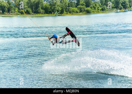 Wakeboarder salta da un trampolino di lancio dietro una corda e rende un'onda sull'acqua. Foto Stock