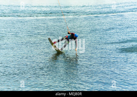 Wakeboarder salta da un trampolino di lancio dietro una corda e rende un'onda sull'acqua. Foto Stock