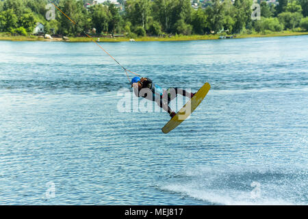 Wakeboarder salta da un trampolino di lancio dietro una corda e rende un'onda sull'acqua. Foto Stock