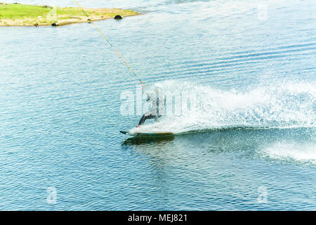 Wakeboarder salta da un trampolino di lancio dietro una corda e rende un'onda sull'acqua. Foto Stock