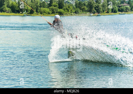 Wakeboarder salta da un trampolino di lancio dietro una corda e rende un'onda sull'acqua. Foto Stock