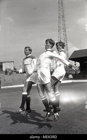 1964, Charlton Athletic FC, foto storiche che mostra tre Charlton Calcio giocatori compreso Billy legami sul passo in corrispondenza della valle, la loro terra, saltando su in mostra il loro nuovo kit calcio. Tra il 1964 e il 1966 il Charlton giocatori indossava una smart tutti i kit bianco rosso con le spalle e la mano e badge sowrd apparve per la prima volta sulla maglietta. Foto Stock