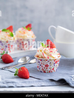 Muffin fatti in casa o i tortini con panna alla vaniglia e fragole fresche su sfondo grigio chiaro, con un copyspace Foto Stock