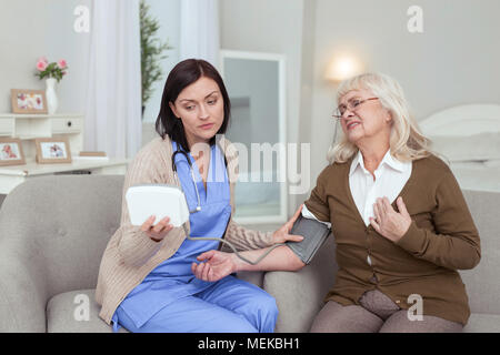 Preoccupato per il caregiver femmina controllando la pressione del sangue Foto Stock