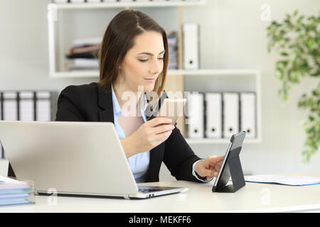 Lavoratore di ufficio lavora con più dispositivi su un computer desktop Foto Stock