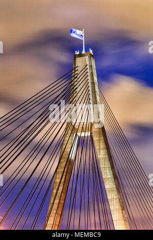 Montante illuminato e arco di Anzac bridge in Sydney con bandiera australiana sventolare nel vento al tramonto contro le nubi e cielo blu Foto Stock