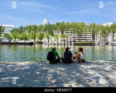 Tre persone sedute in zona ombreggiata lungo il Canal Villette avente un picnic con vino su un bel pomeriggio di sole in aprile. Parigi, Francia. Foto Stock