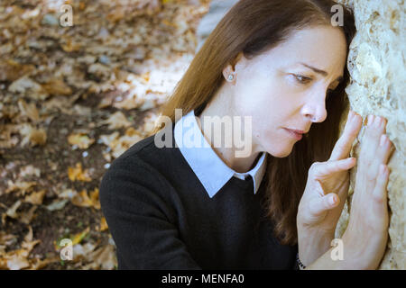 Ritratto di donna, triste, guardando verso il basso e con le sue mani su una parete, all'aperto. Foto Stock