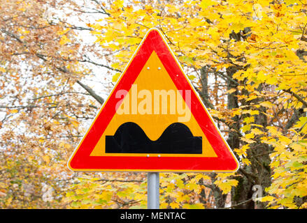 Su strada dissestata segno giallo su foglie di autunno sfondo Foto Stock