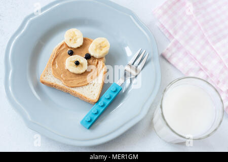 Burro di arachidi e banana toast in Orsacchiotto forma e bicchiere di latte di mandorla. Funny arte cibo per bambini. Vista dall'alto. Mangiare sano concetto Foto Stock