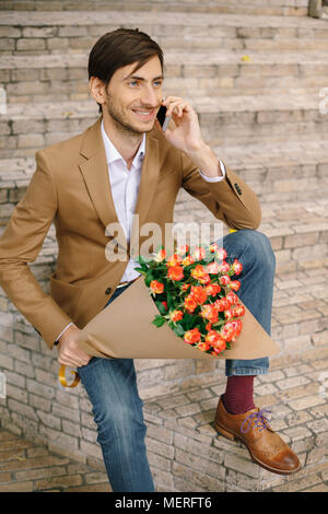 Uomo bello holding bouquet di rose parlando felice sul telefono Foto Stock