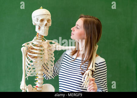 Femmina fresco di alta scuola studente ritratto con un artificiale umana dello scheletro del corpo. Studente divertirsi nella classe di biologia. Il concetto di istruzione. Foto Stock